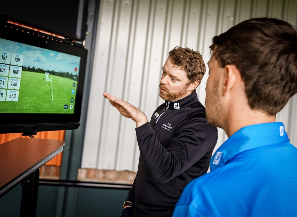 Golf coach showing a player their swing stats on a TrackMan range monitor at The Shropshire Golf Club in Telford, part of individual golf coaching and TrackMan driving range in Telford