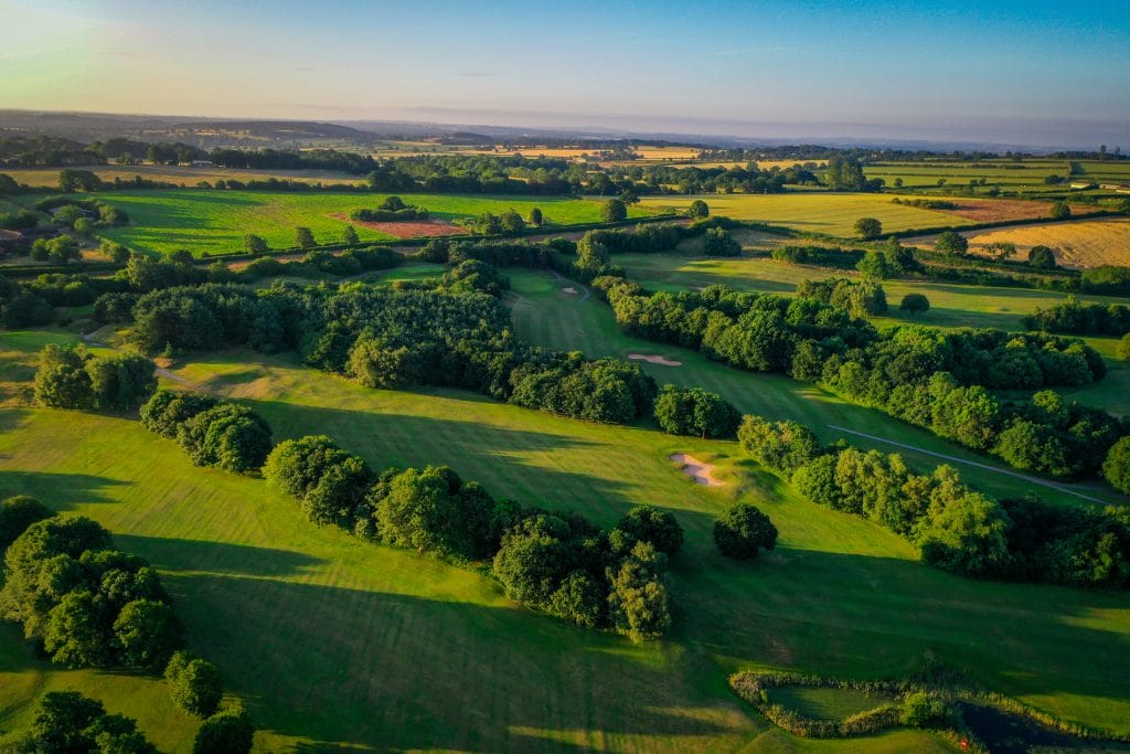 Aerial view of The Shropshire Golf Club at sunset, highlighting the 18 hole golf course in Telford with rolling hills and natural beauty
