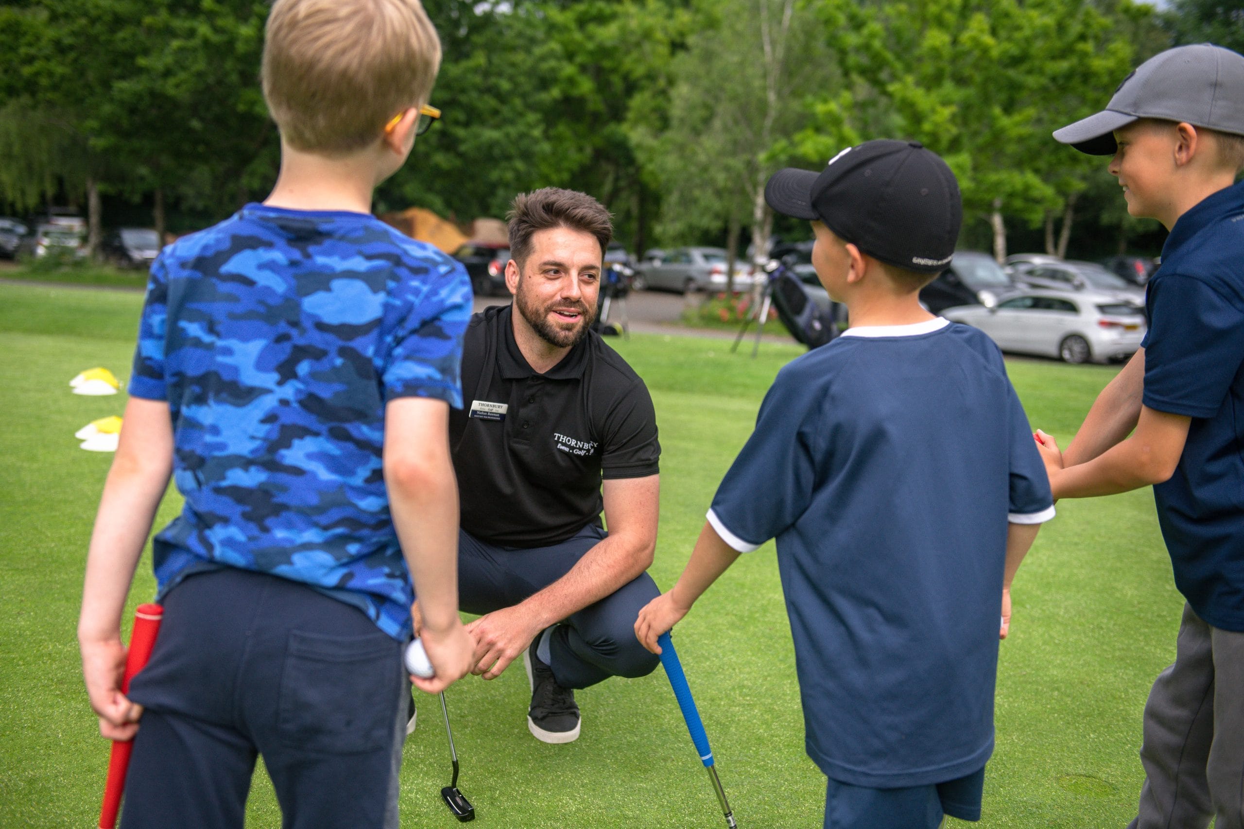 Golf coach kneeling to talk to young golfers during a junior golf lesson at The Shropshire Golf Club in Telford, part of junior golf coaching in Telford